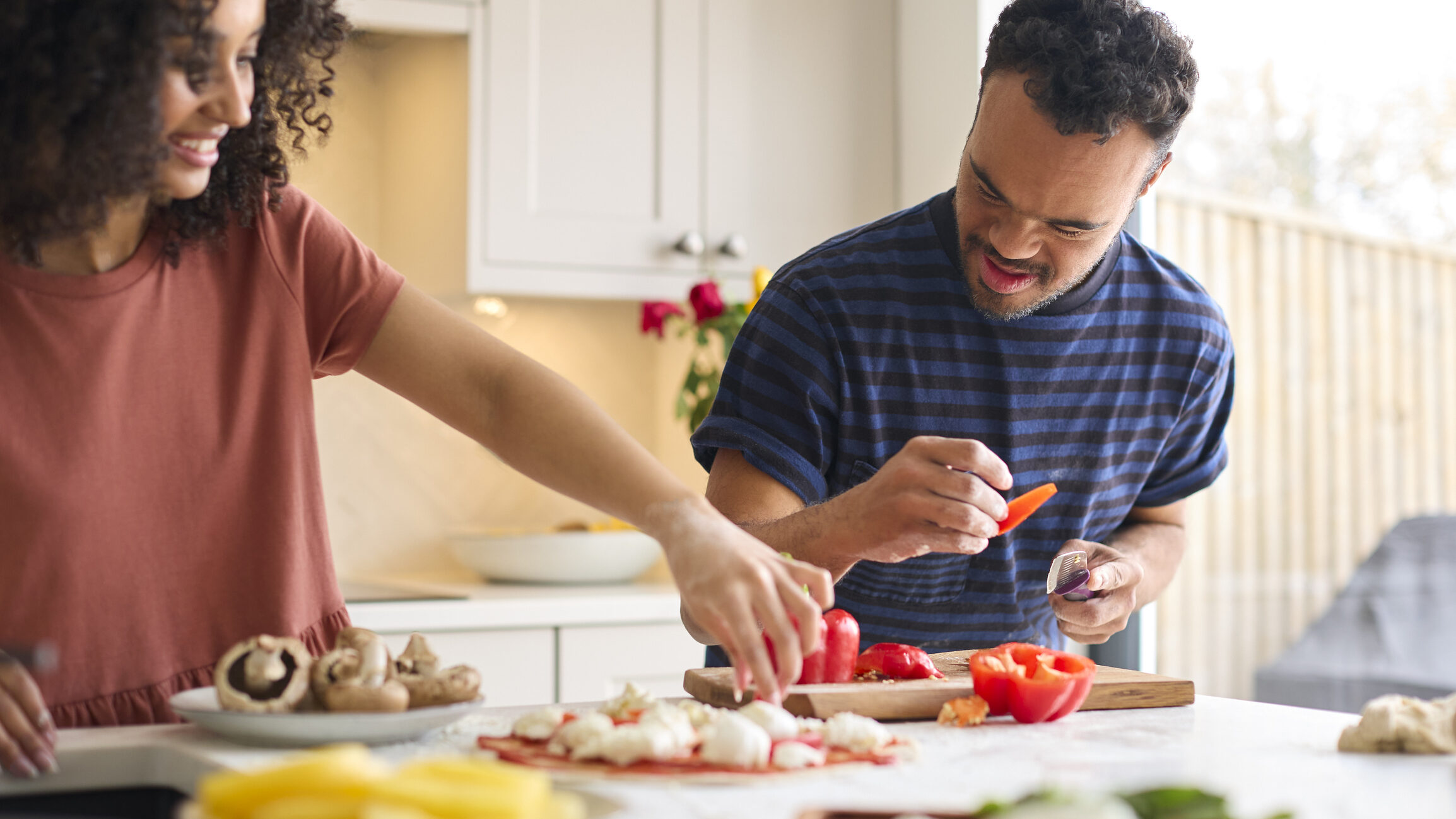 Couple At Home With Man With Down Syndrome And Woman Preparing Topping For Pizza In Kitchen Together
